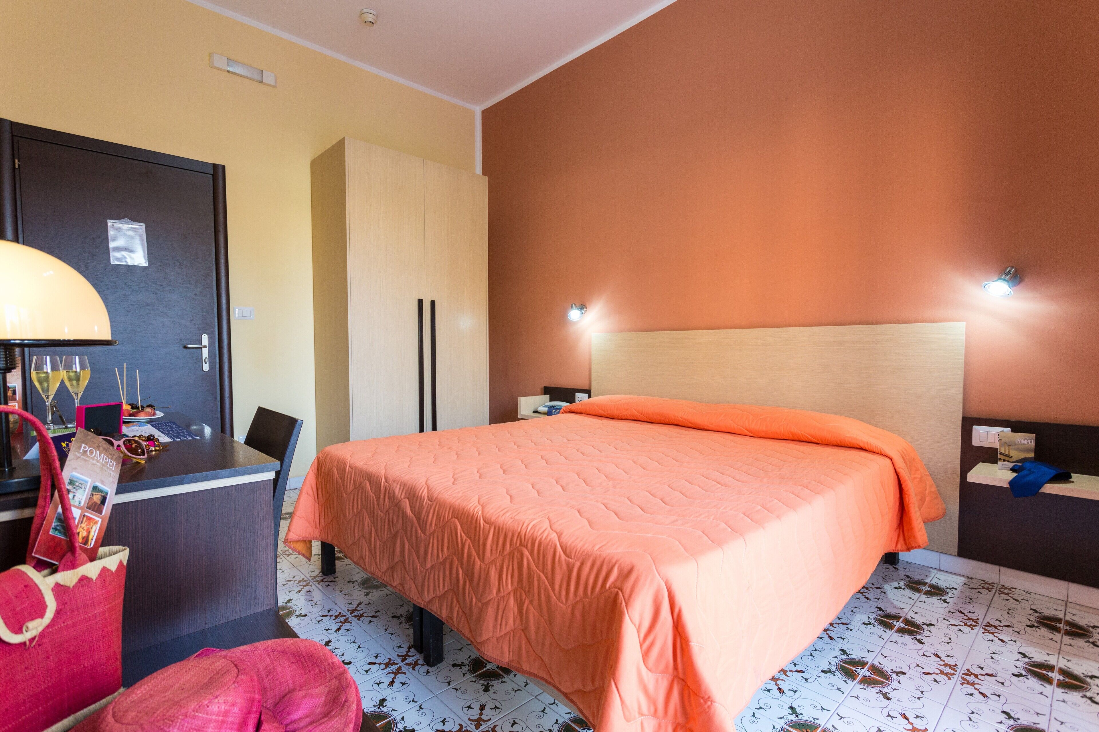 Una habitación de hotel con una cama, un escritorio, una silla, una lámpara y una puerta.