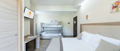 A hotel room with a bunk bed, a desk, and a bed with pillows.