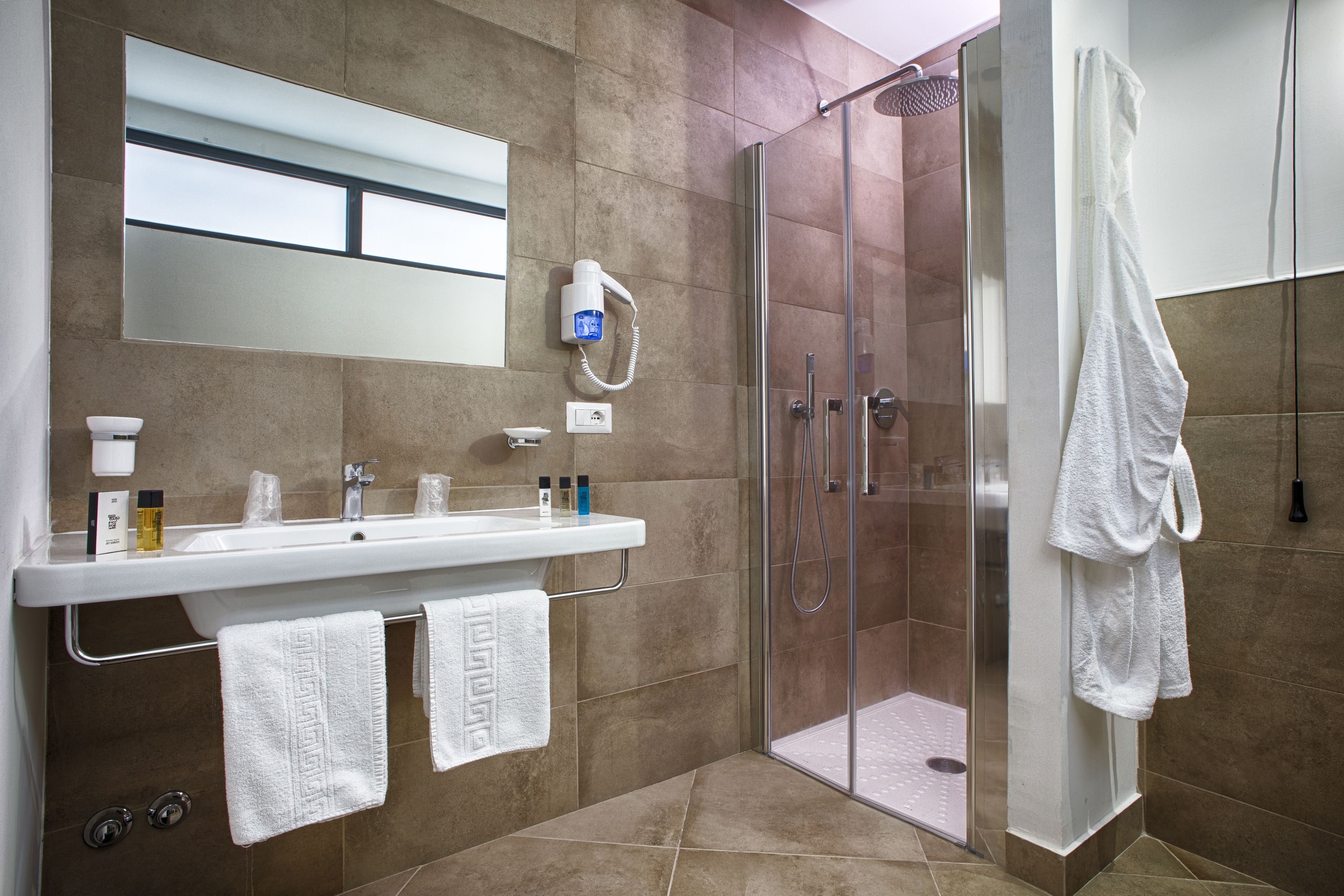 A modern bathroom with a glass-enclosed shower, a white sink with a mirror above it, and two towels hanging on a rack.