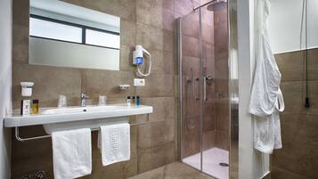A modern bathroom with a glass-enclosed shower, a white sink with a mirror above it, and two towels hanging on a rack.