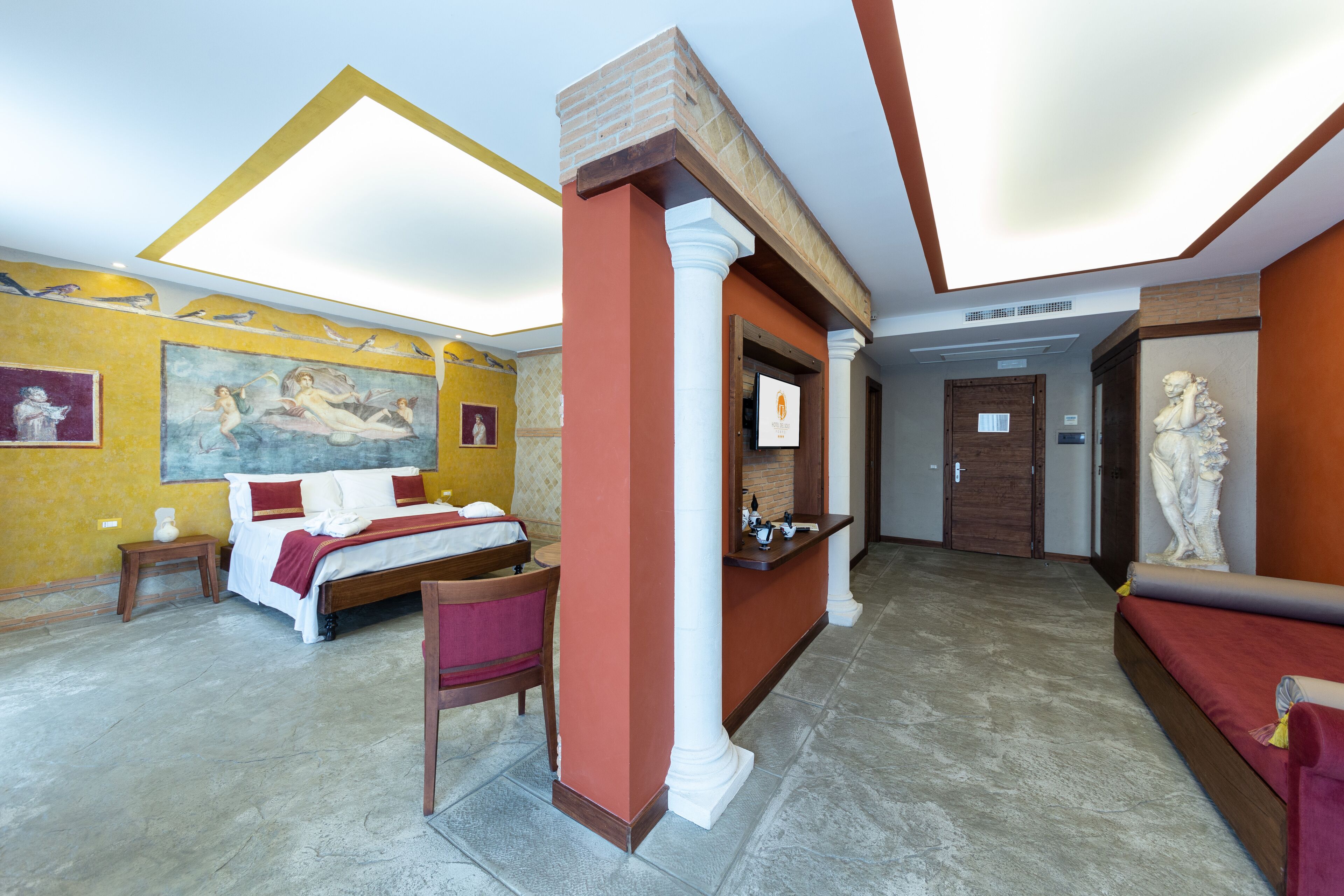 Ein Hotelzimmer mit Bett, Sitzgelegenheit, Badezimmer und einem Flur mit einer Statue.
