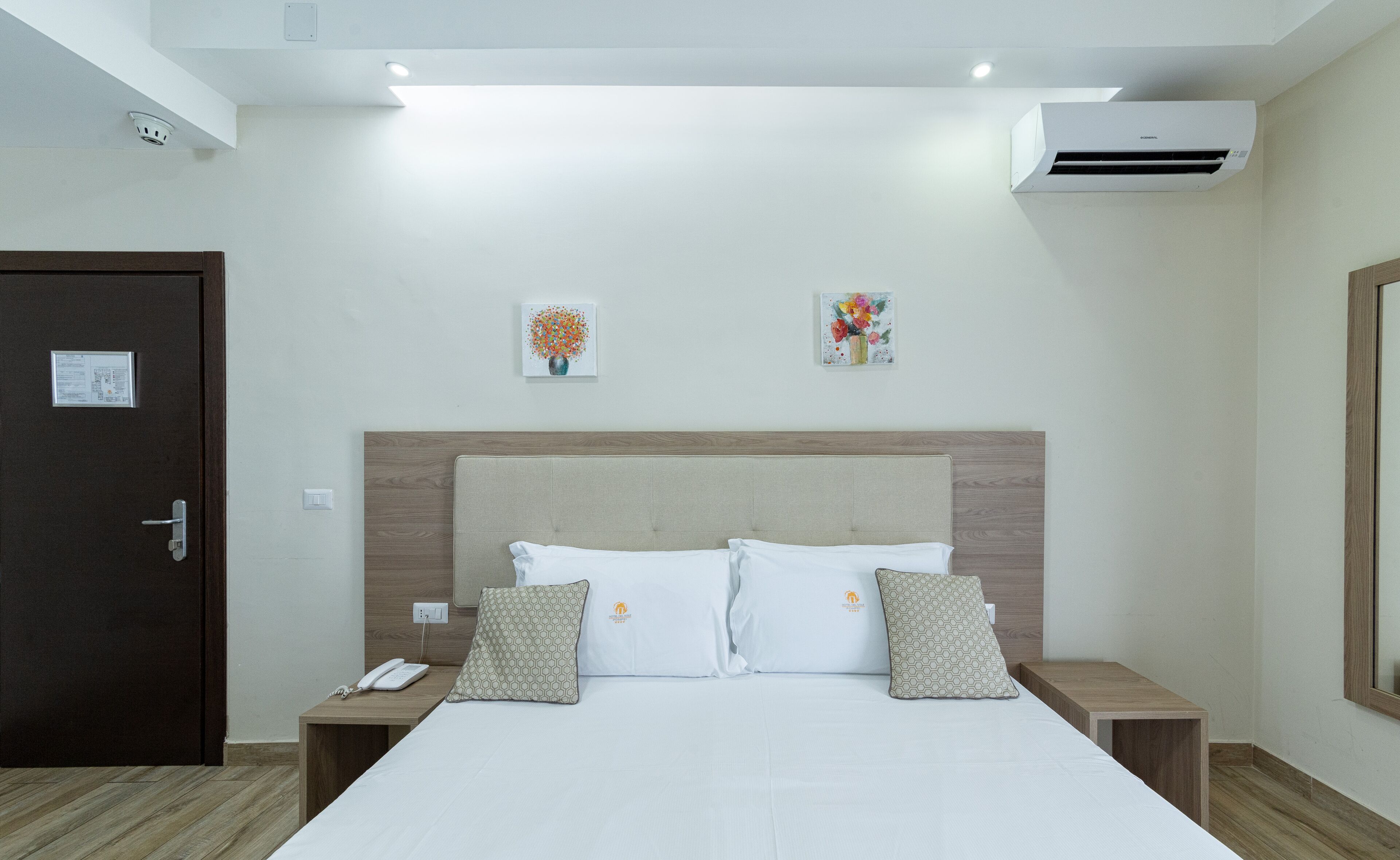 A hotel room with a bed, two bedside tables, a telephone, and an air conditioning unit.