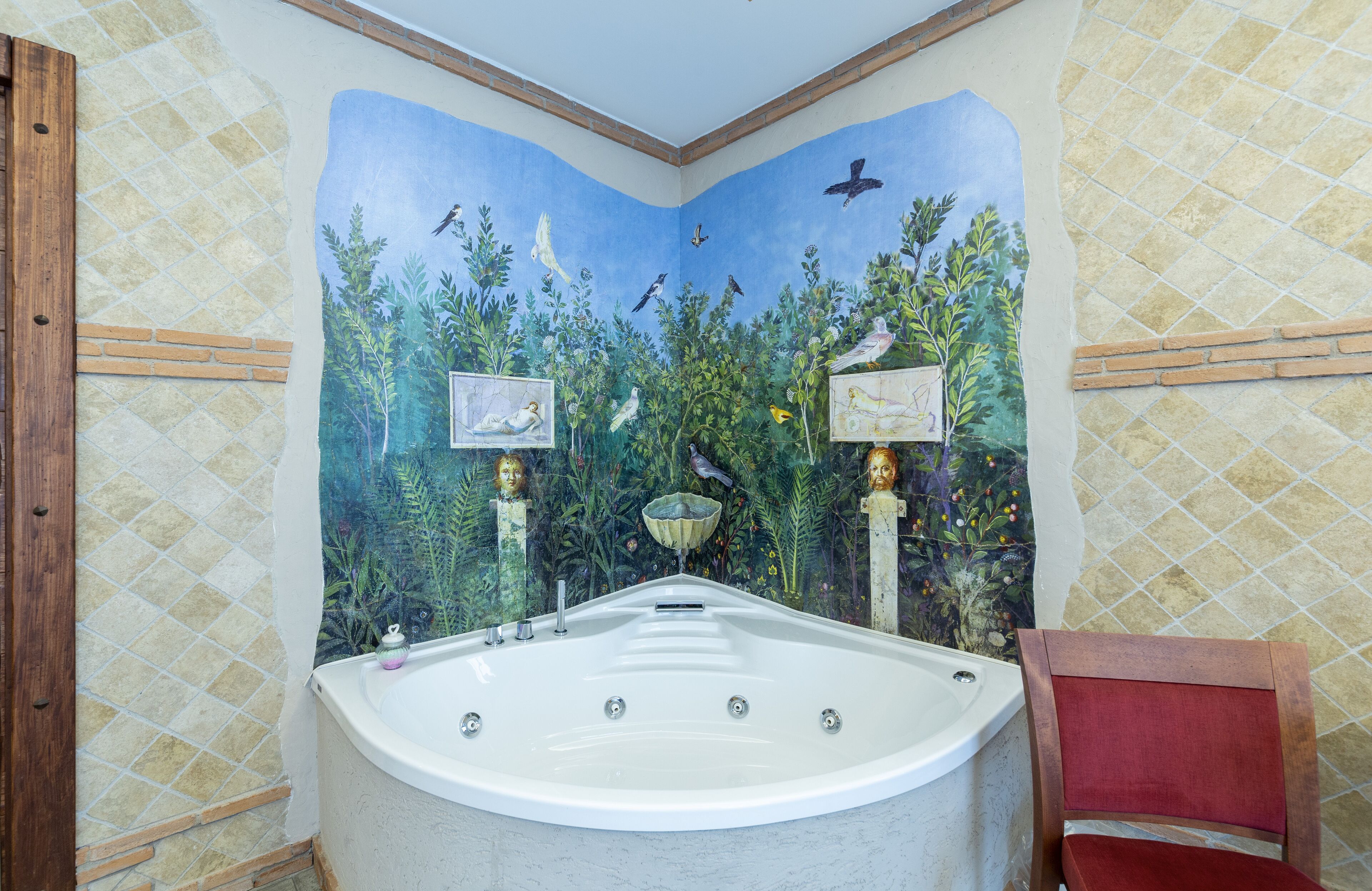 Un baño con una bañera grande, una silla de madera y un mural con aves y árboles en la pared.