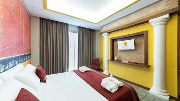 A hotel room with a large bed, a television mounted on the wall, and a red chair.