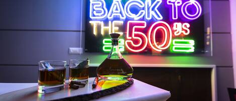Un bar con un letrero de neón, dos vasos de whisky y una botella de whisky Amosite sobre una mesa.