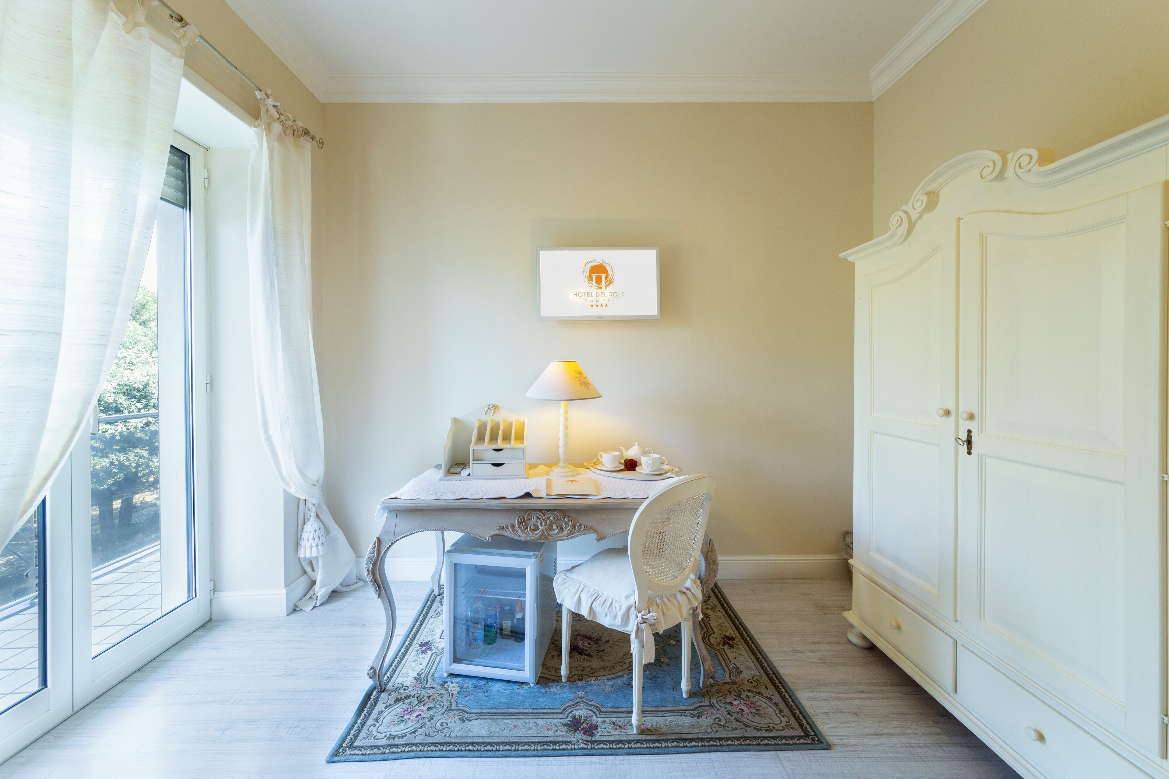 A hotel room with a dining table, a chair, a lamp, a small cabinet, and a wardrobe.