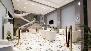 Een ruime lobby met betegelde vloer, een trap en een zithoek met witte stoelen en een bank.