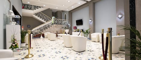 Un vestíbulo amplio con suelo de baldosas, una escalera y una zona de estar con sillas blancas y un sofá.