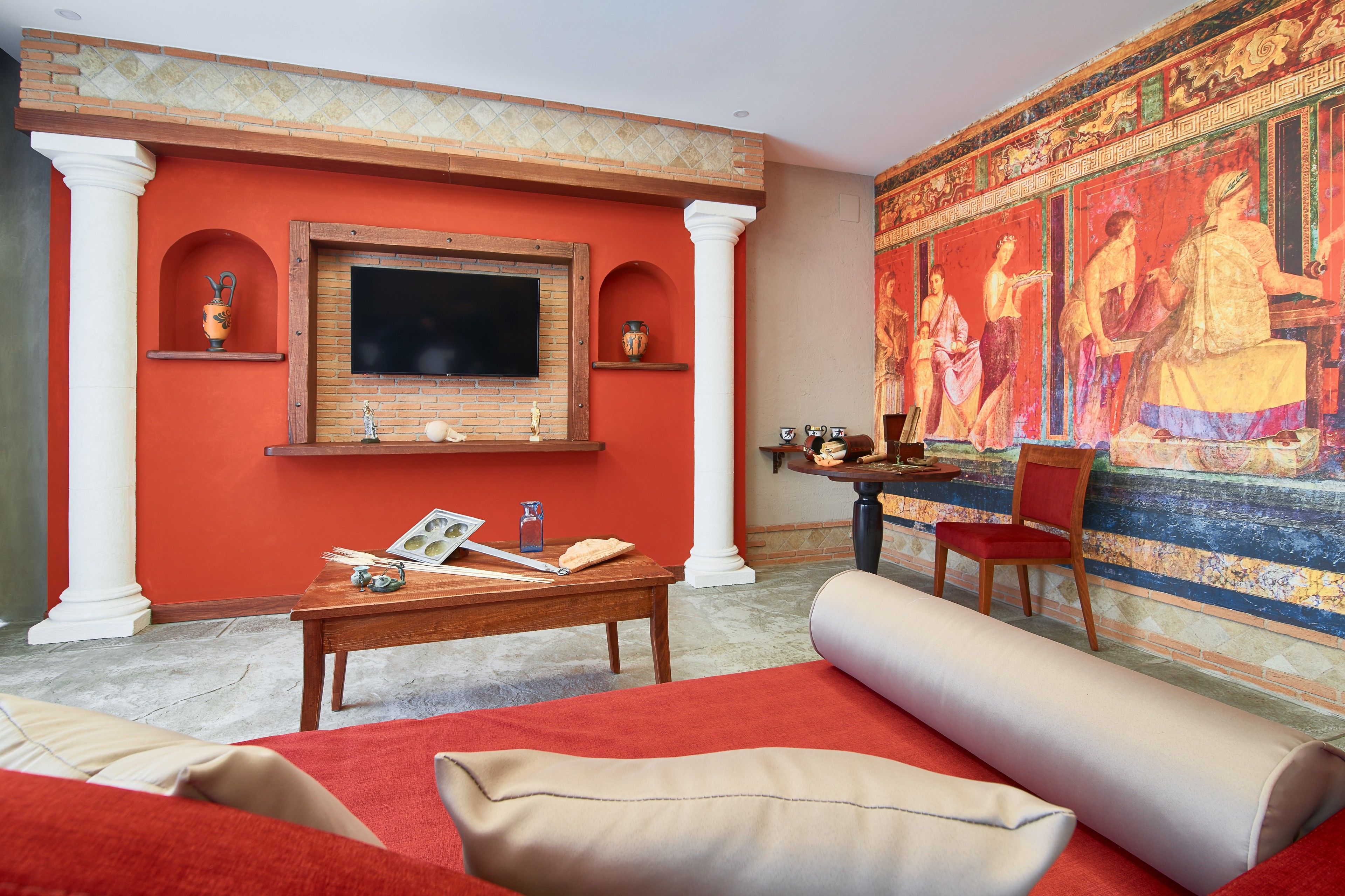 A living room with a red wall, a large mural, a television, and a wooden coffee table with books and a vase.
