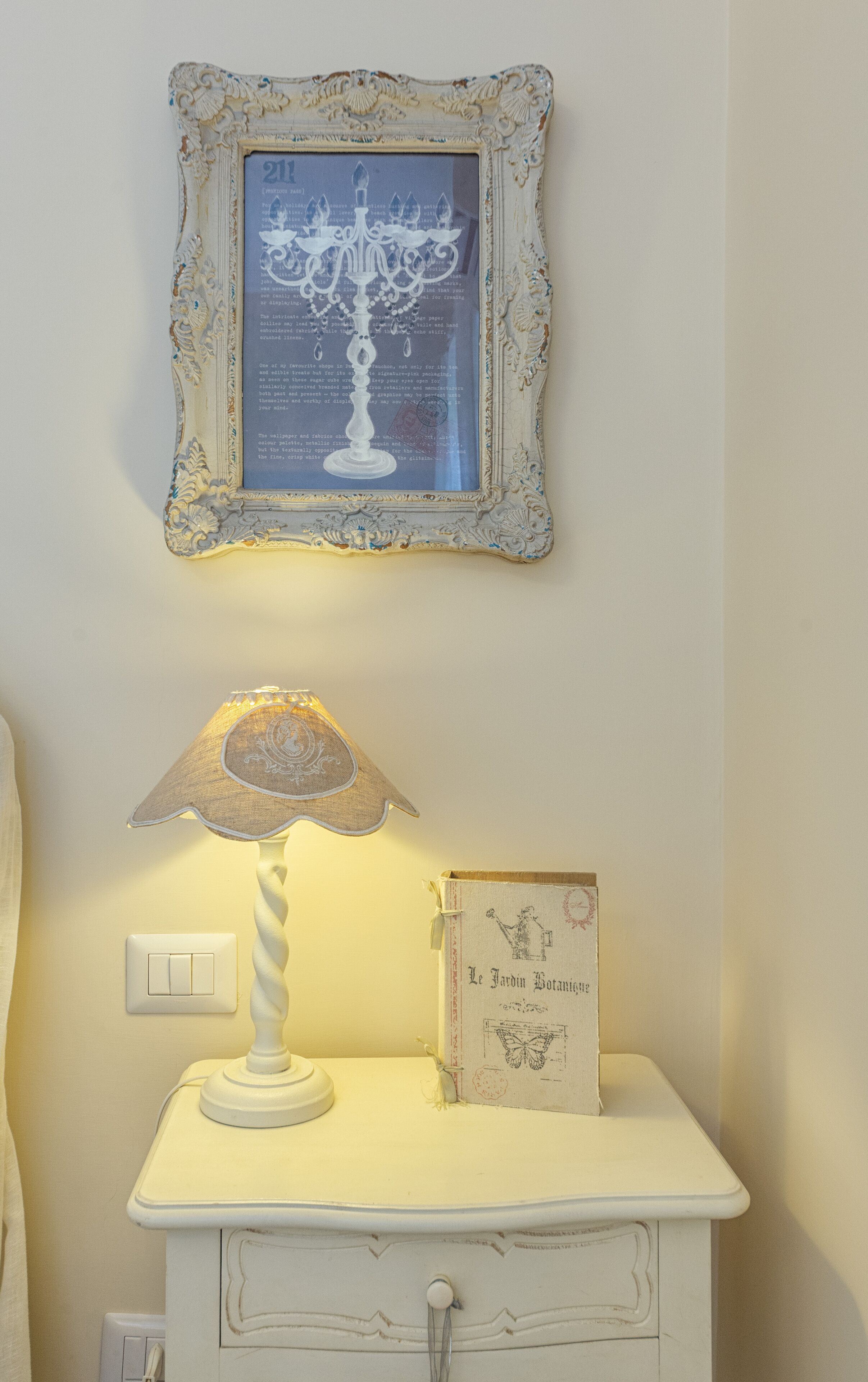 A bedside table with a lamp, a framed picture, and a book titled "Le Jardin Botanique".