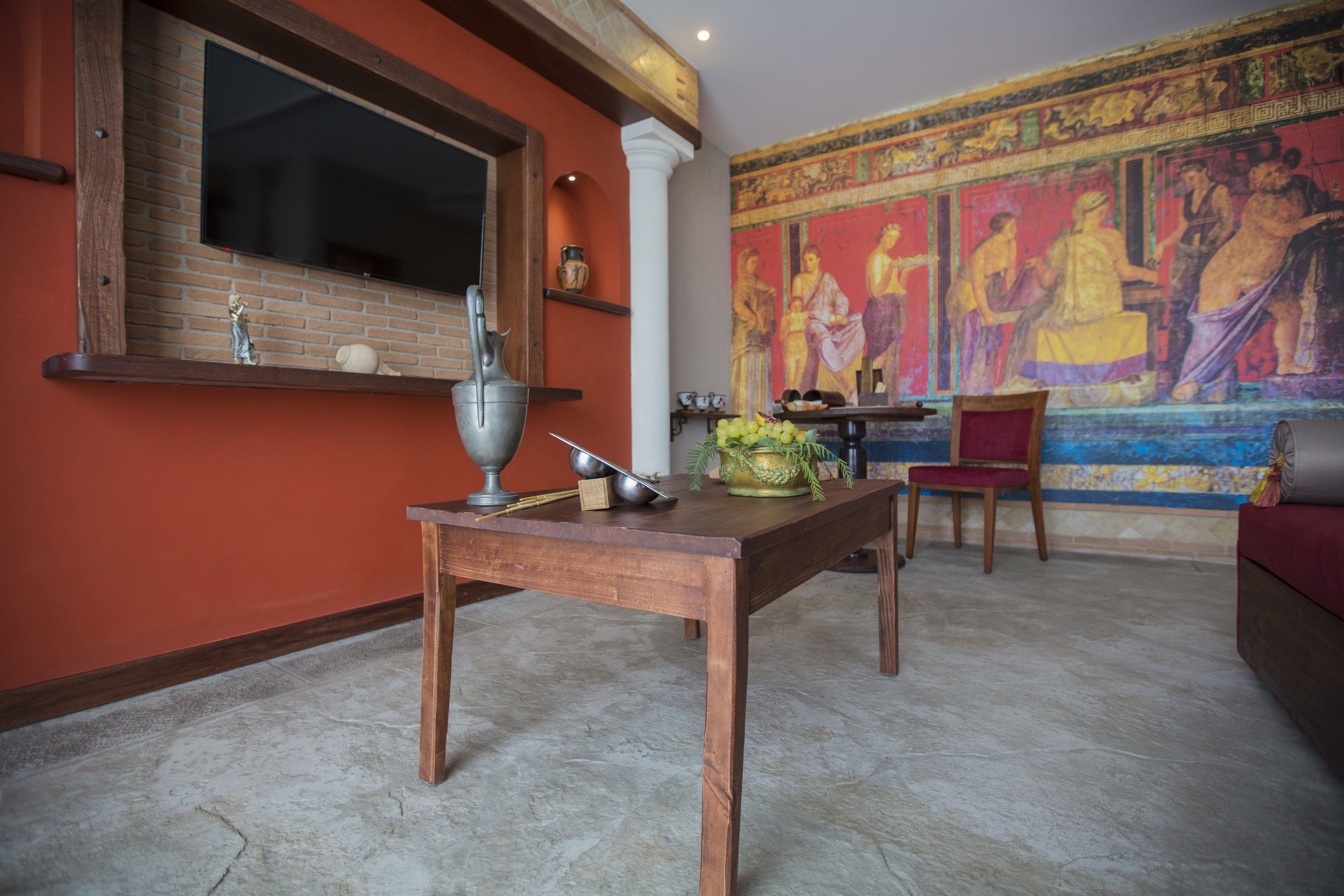Una habitación con pared de ladrillo, televisor de pantalla plana, mesa de madera, una silla roja y un mural colorido.