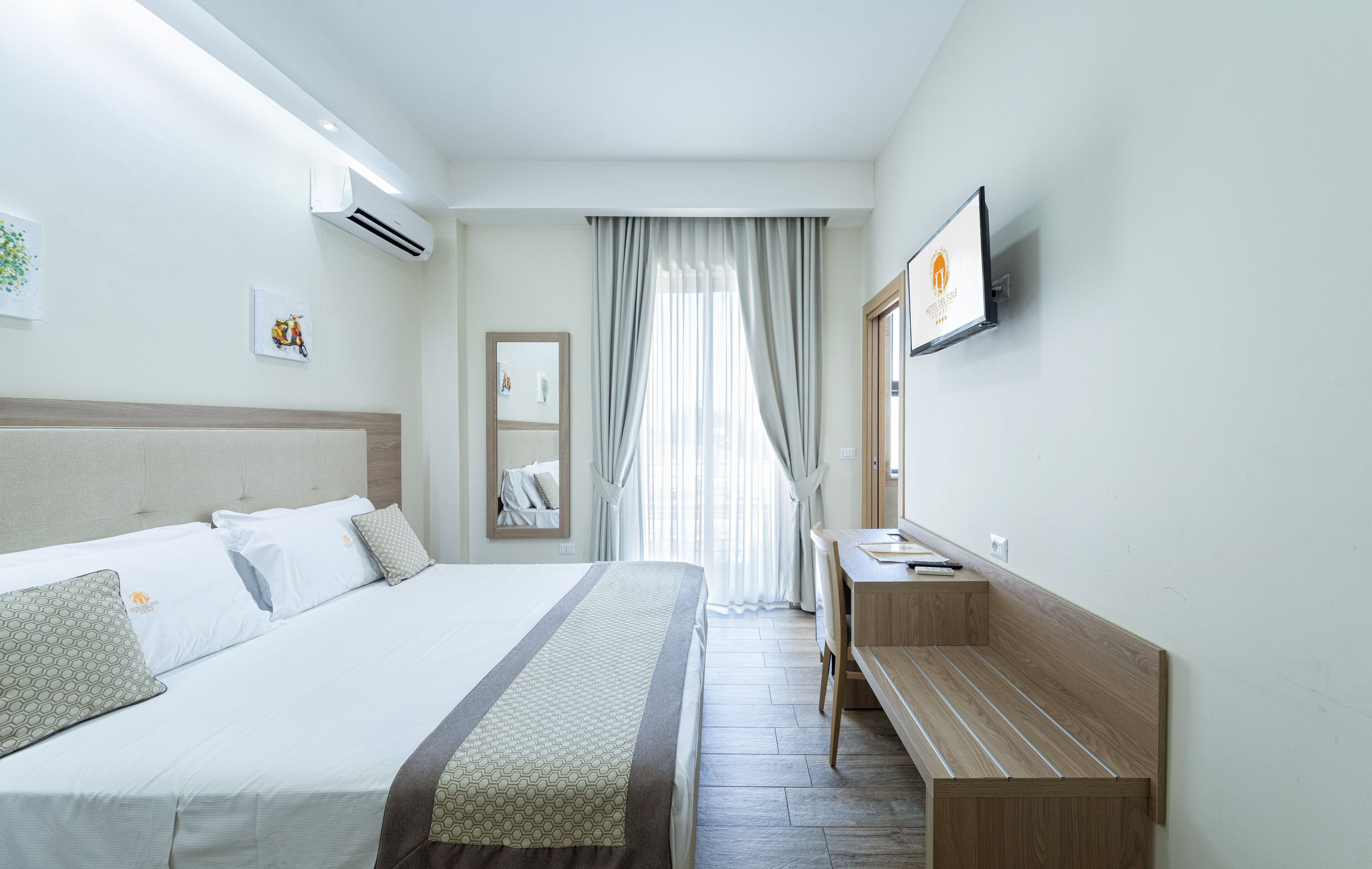 A hotel room with a bed, a desk, a chair, a TV, and a window with curtains.