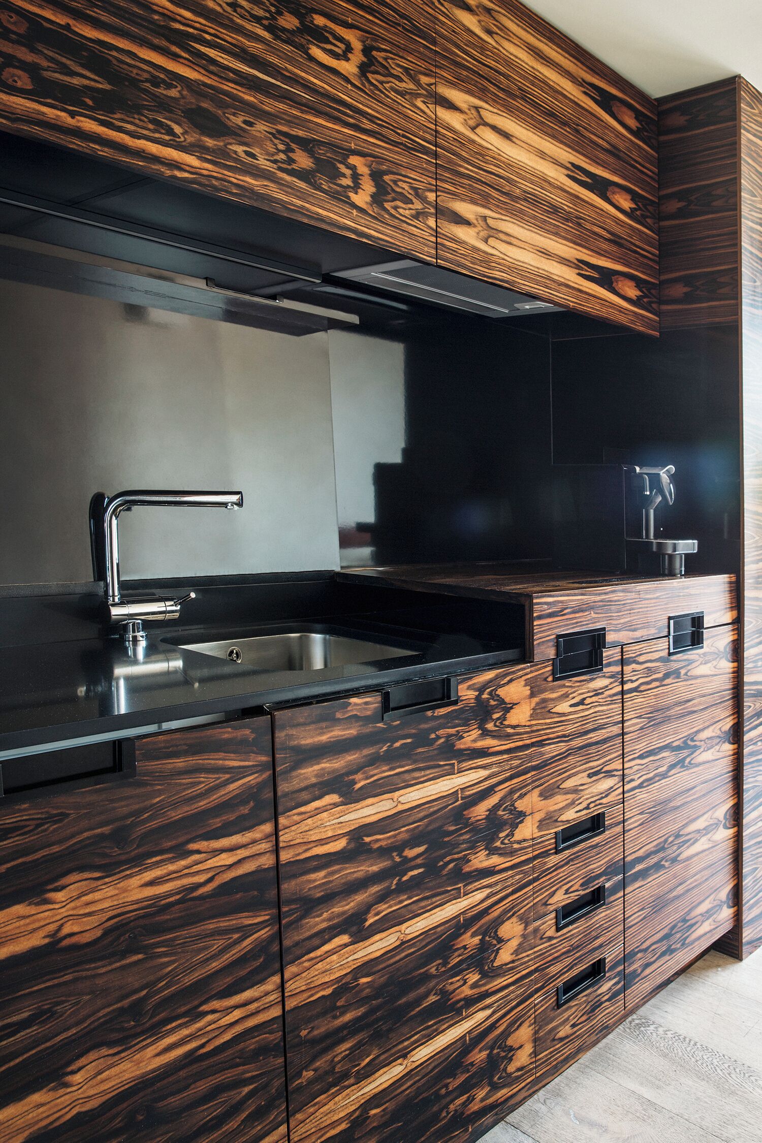 Une cuisine moderne avec un plan de travail noir, un évier en acier inoxydable et des meubles de rangement en bois.
