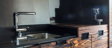 A modern kitchen with a black countertop, stainless steel sink, and wooden cabinetry.