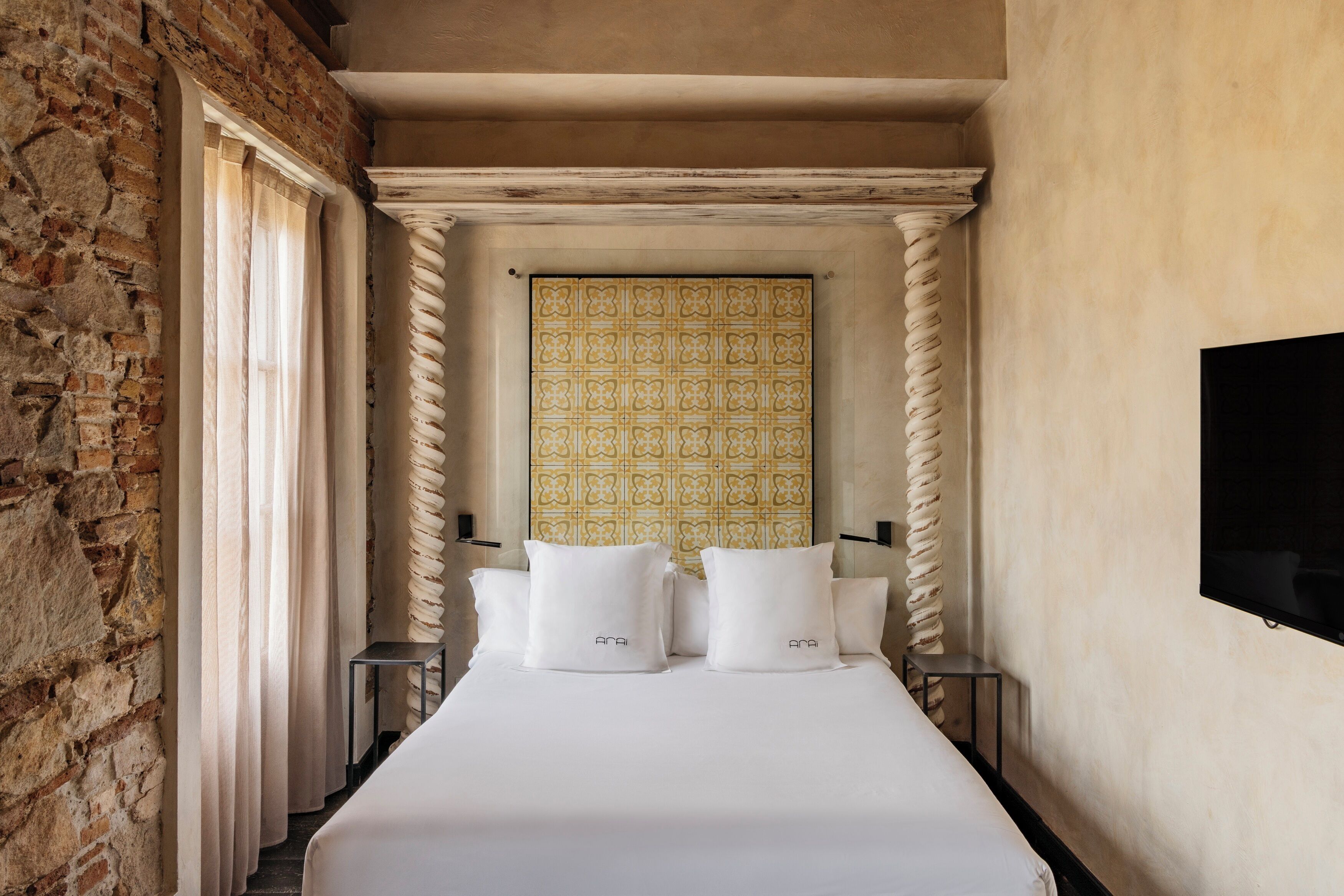 Habitación de hotel estrecha con una cama, dos almohadas, un televisor y un papel tapiz estampado.