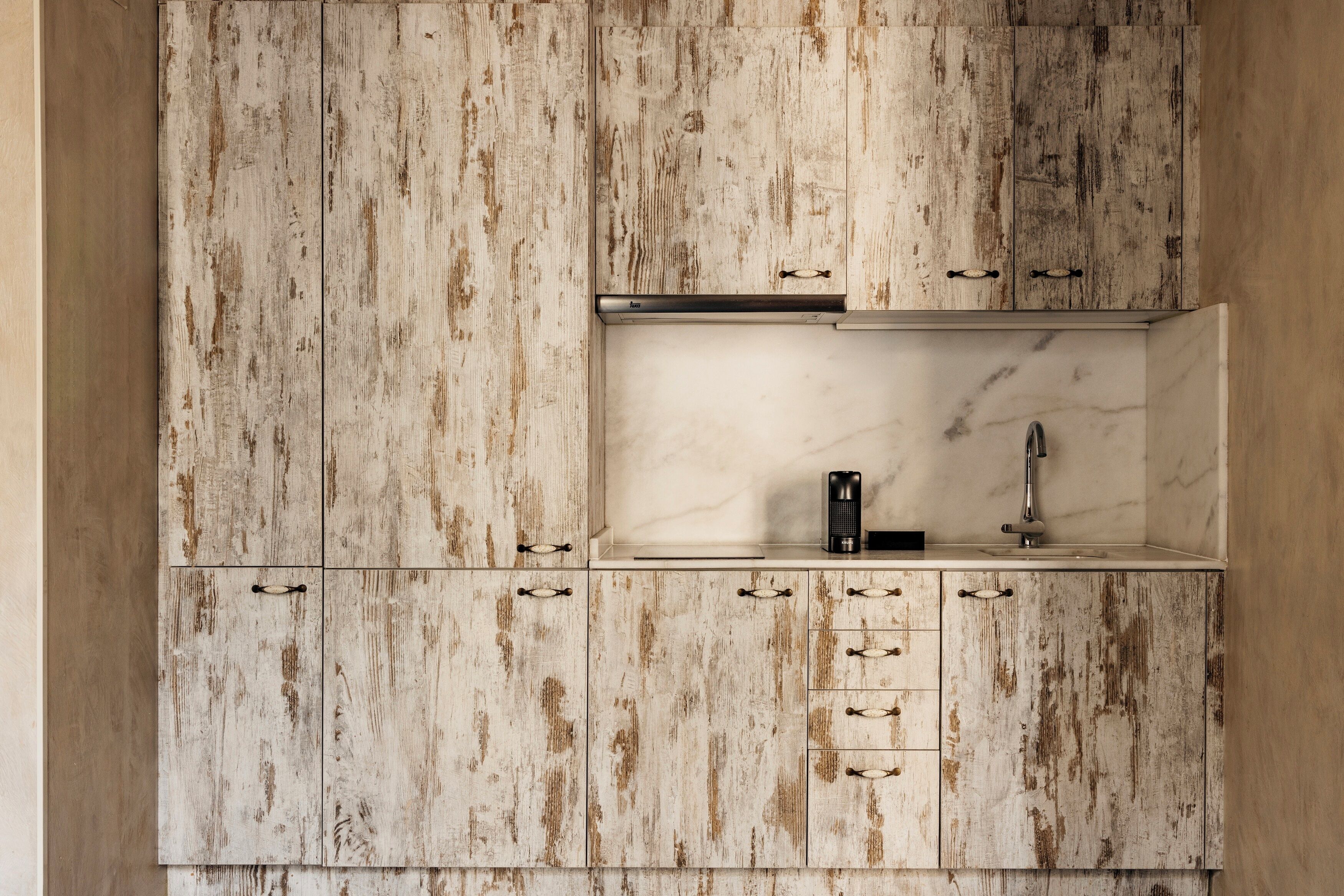 Une cuisine dotée de meubles en bois rustique, d’un plan de travail en marbre et d’un robinet moderne.