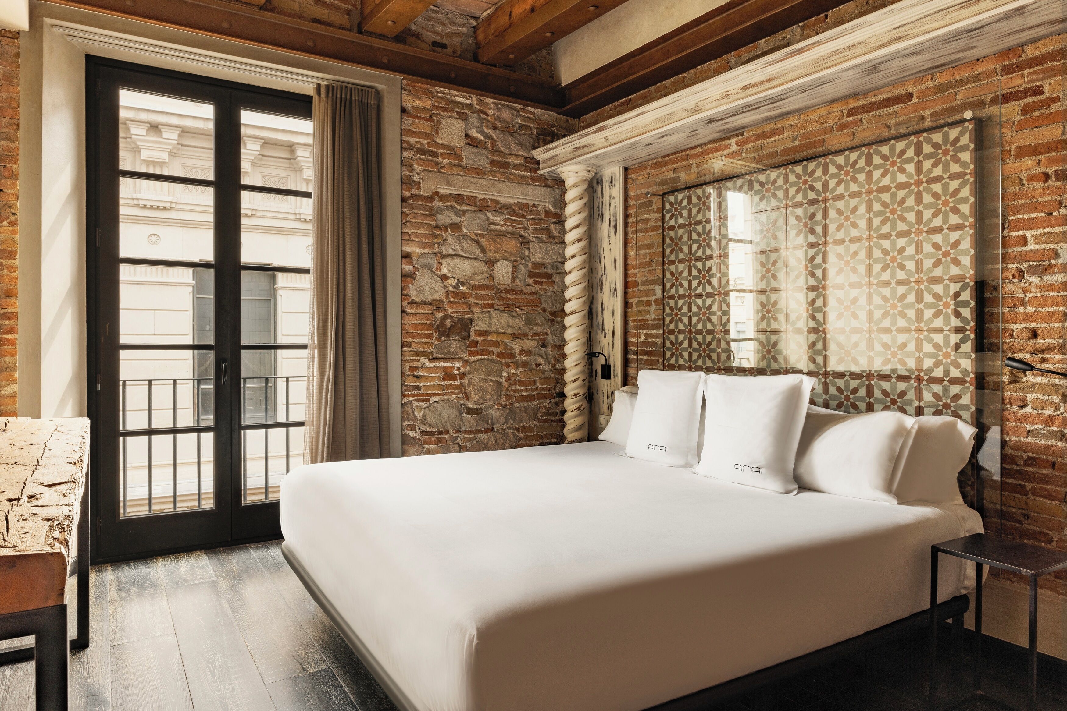 A bedroom with a large bed, a wooden bench, a stone wall, and a patterned wall panel.
