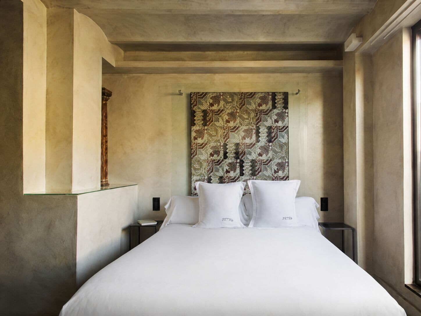 A hotel room with a large bed, a patterned headboard, and a nightstand with a lamp.