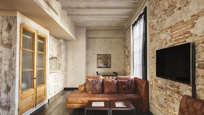 A living room with a brick wall, a sofa, a television, and a wooden cabinet. - Arai Aparthotel (Barcelona)