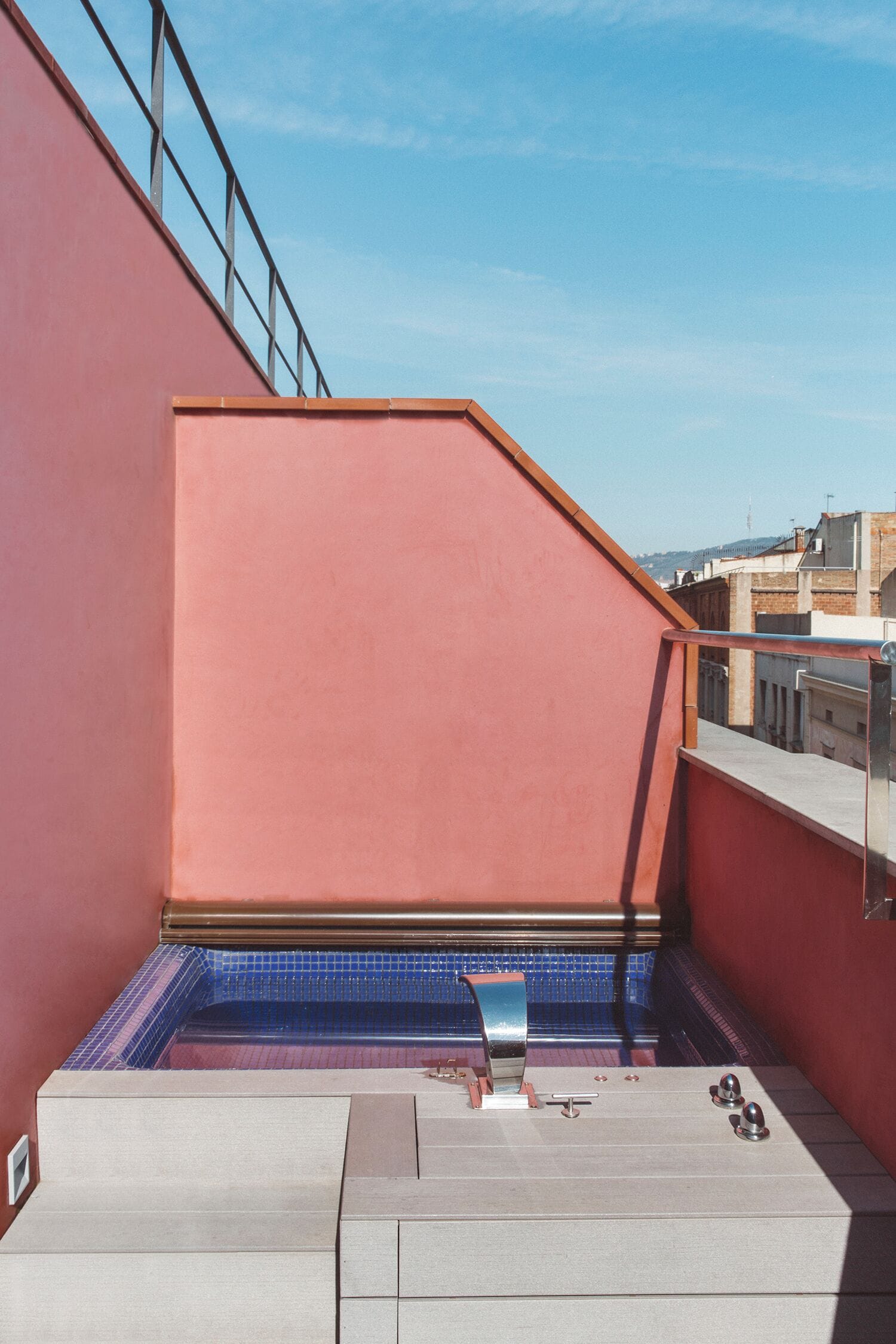 Una piscina en la azotea con un muro rojo y una barandilla metálica.