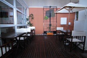 Un patio al aire libre con mesas y sillas de madera, una sombrilla blanca y una reja de metal.