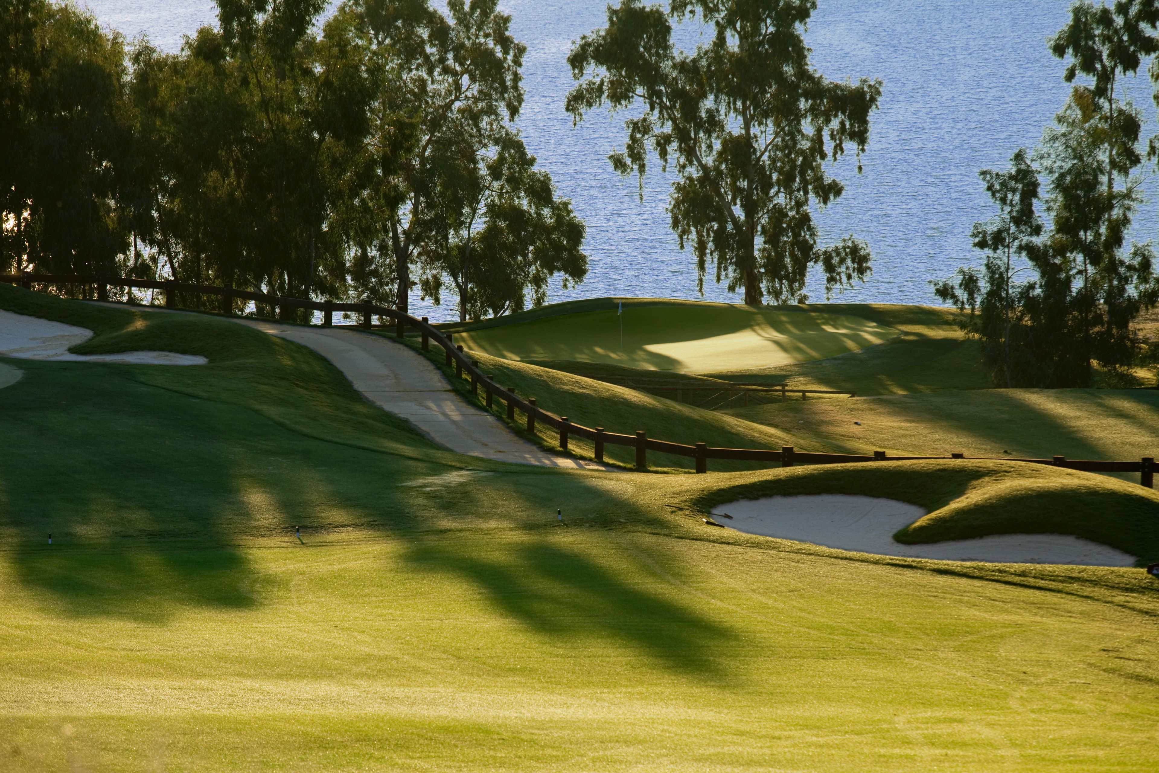 Campo de golf con búnkeres de arena, valla de madera y árboles.