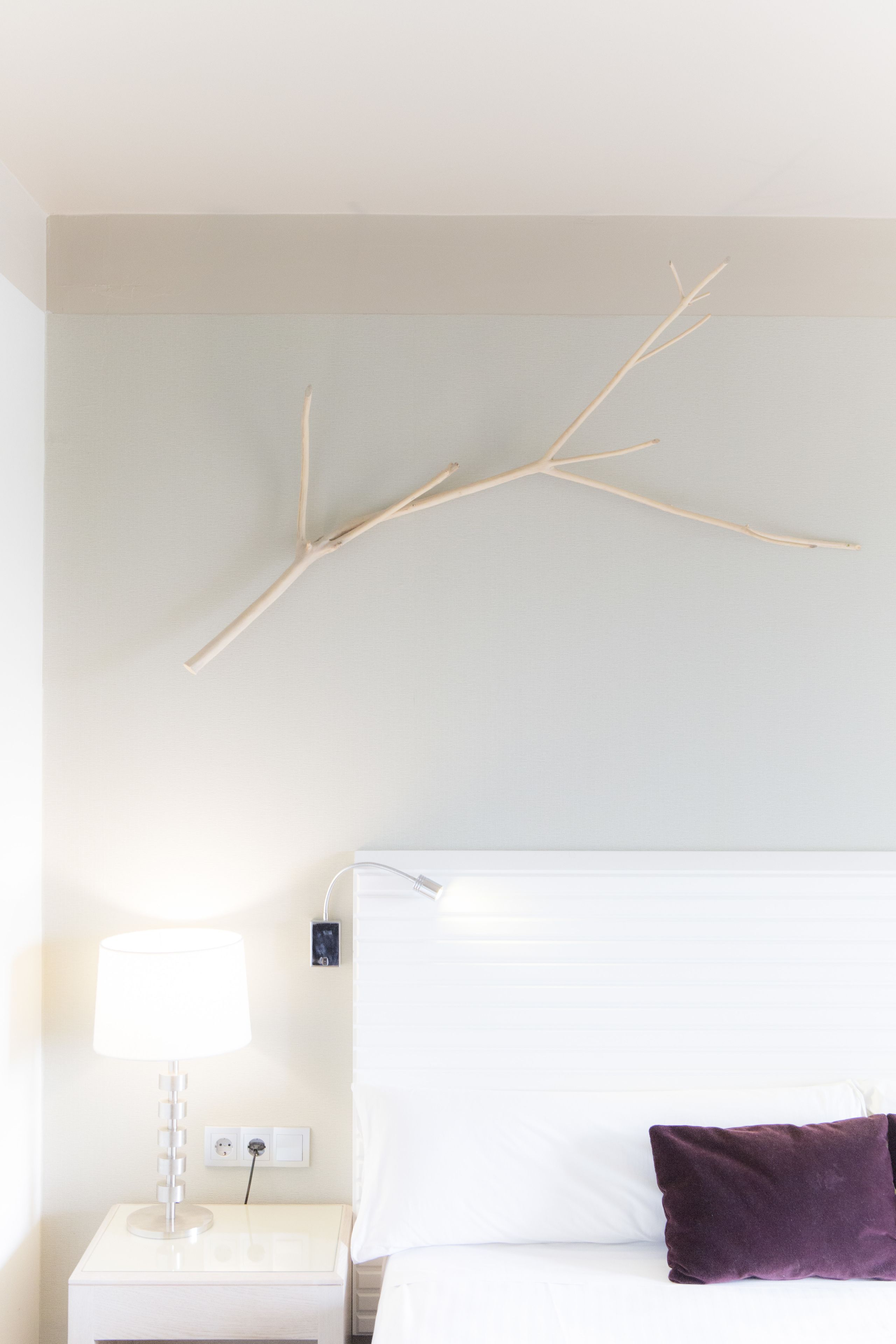 Una habitación de hotel con cama, mesita de noche, lámpara y una decoración floral en la pared.