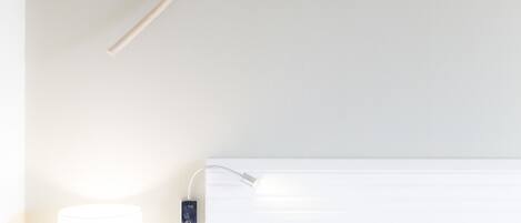 Una habitación de hotel con cama, mesita de noche, lámpara y una decoración floral en la pared.