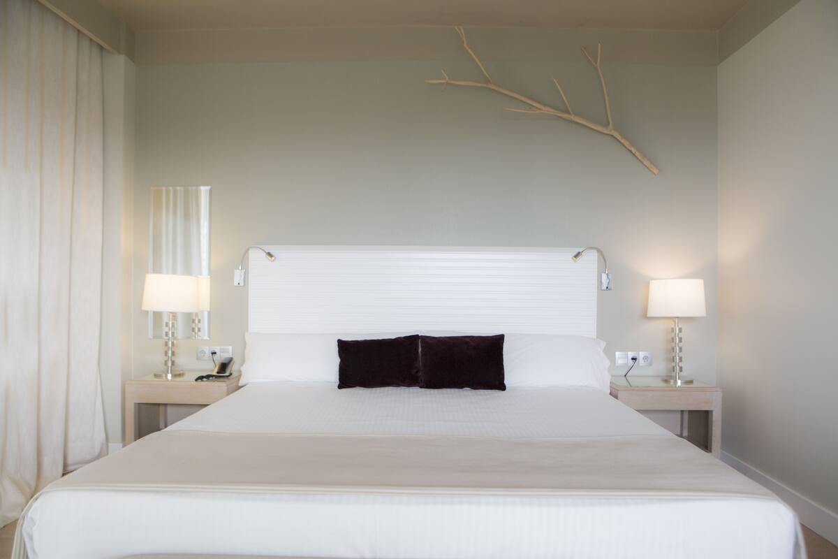 A large bed with white linens, two bedside tables with lamps, and a branch decoration on the wall.