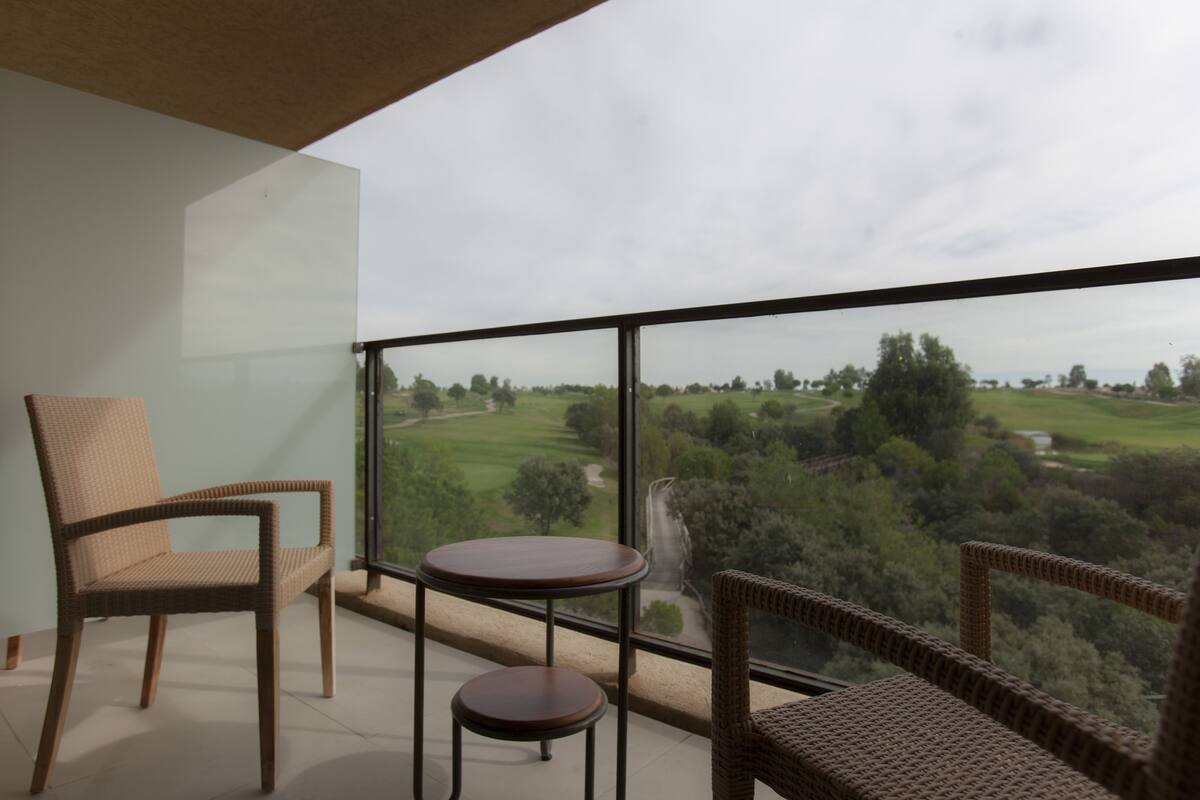 A balcony with wicker furniture, including chairs and a small table, overlooking a golf course.