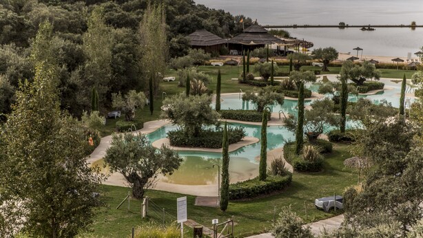 A resort with multiple swimming pools, a golf course, and a view of a lake and mountains.