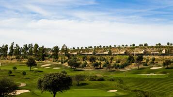 A golf course with sand bunkers, trees, and a clear sky.