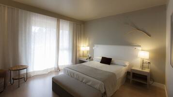 A hotel room with a large bed, a bedside table, a chair, and a window with curtains.