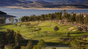 A golf course with a water body in the background, surrounded by hills and trees.