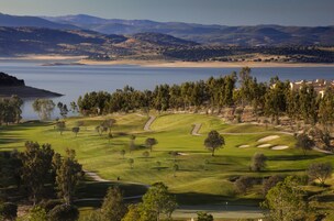 Un campo de golf con un cuerpo de agua al fondo, rodeado de colinas y árboles.