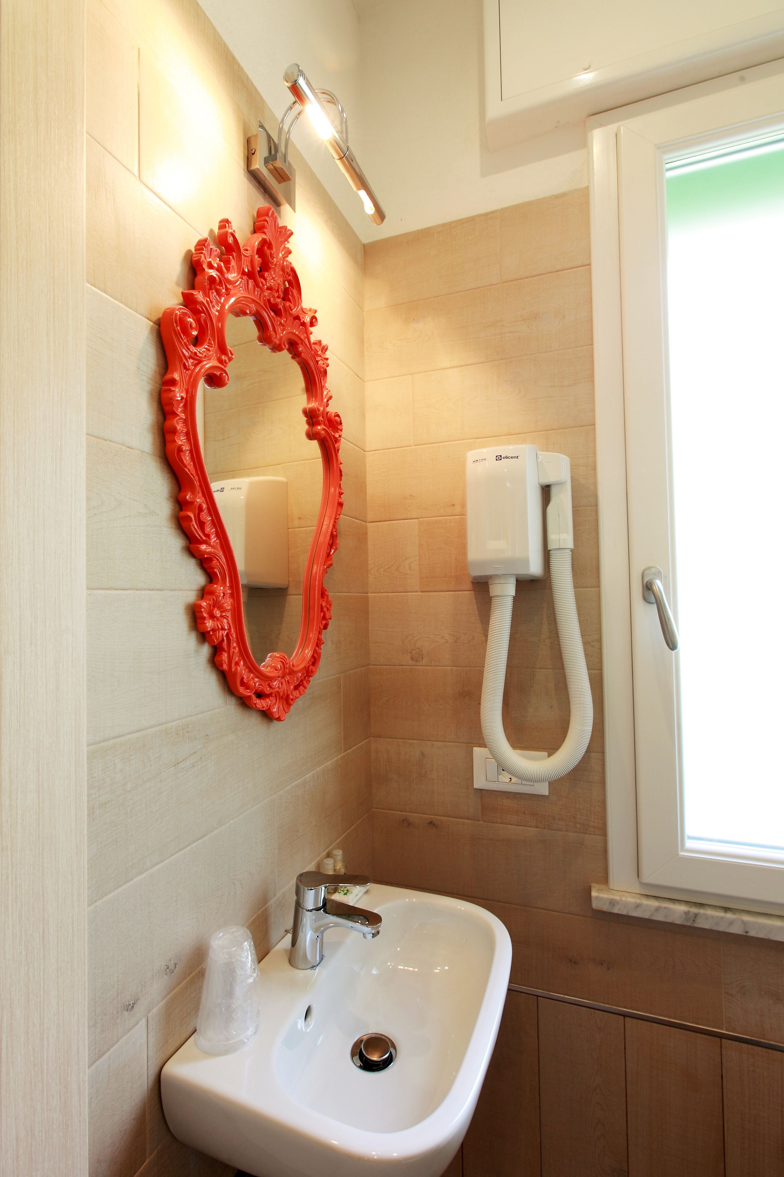 Un baño con un lavabo blanco, un espejo ornamentado rojo, un cabezal de ducha de mano y una ventana con vistas.