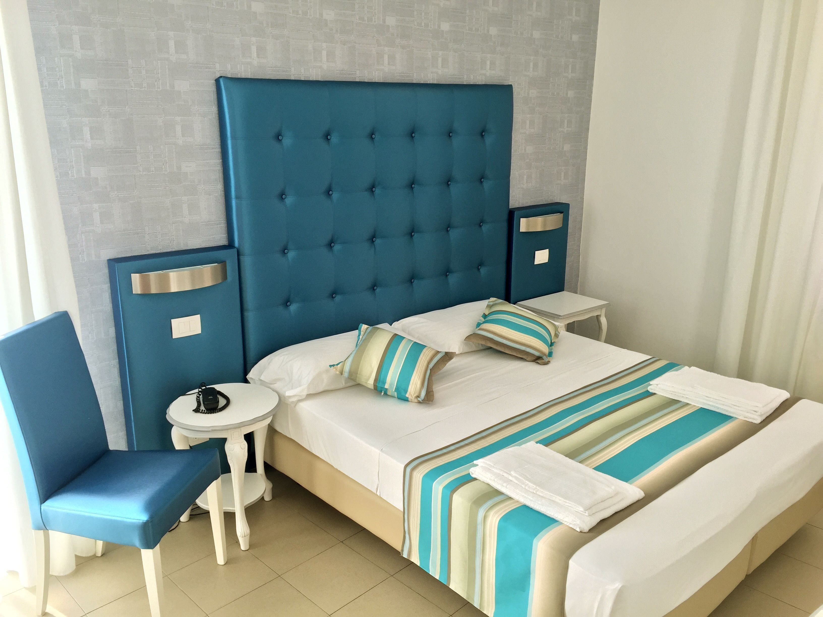A hotel room with a large bed, a chair, a small table, and a nightstand.