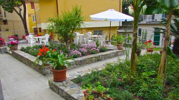 An outdoor patio with stone steps, potted plants, and white plastic chairs.