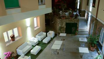 A multi-level indoor courtyard with white sofas, clear glass tables, and potted plants.