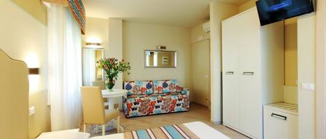 A hotel room with a bed, a sofa, a TV, a desk, and a mirror.