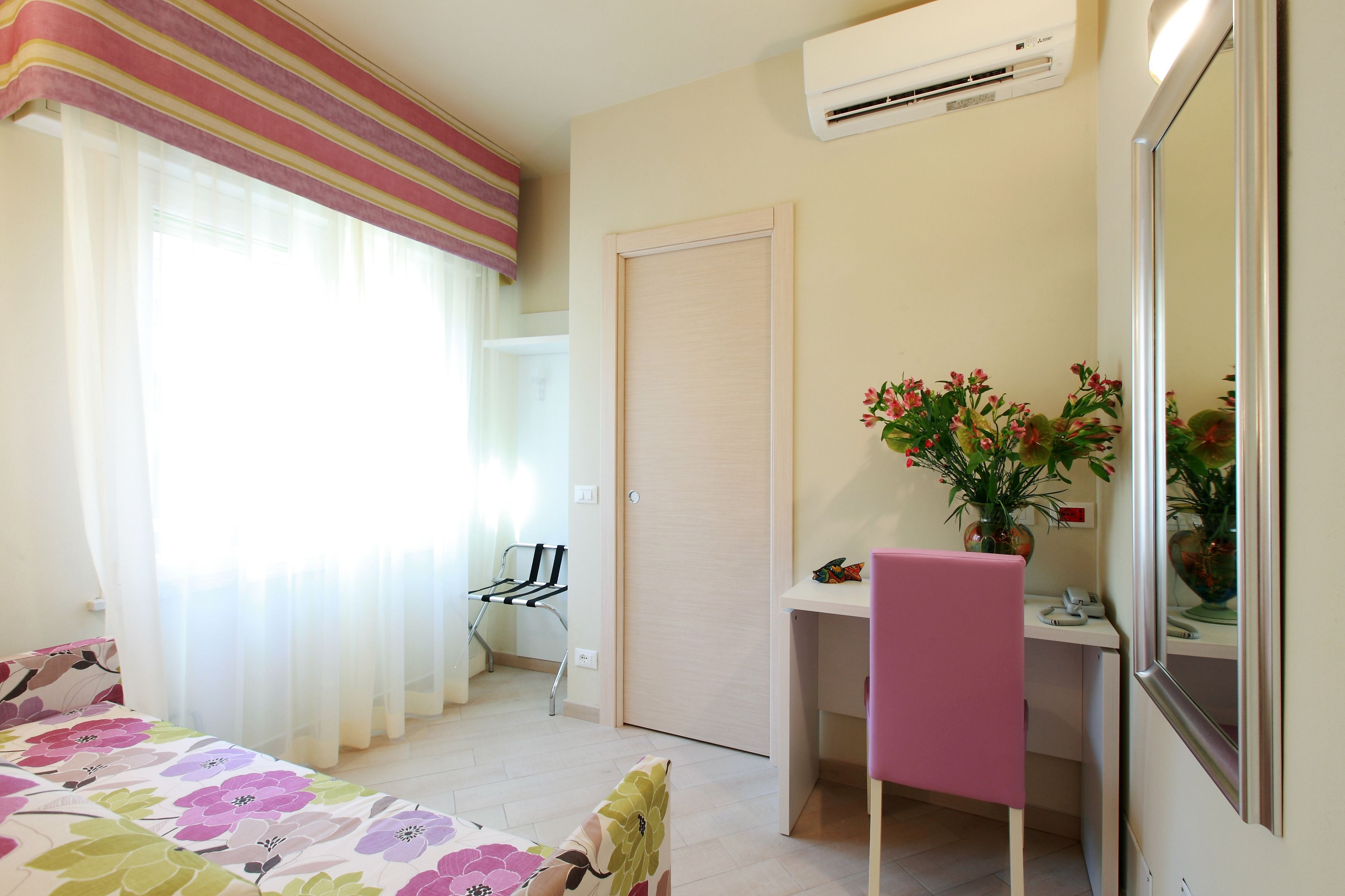 A bedroom with a bed, a desk, a chair, a mirror, and a window with curtains.