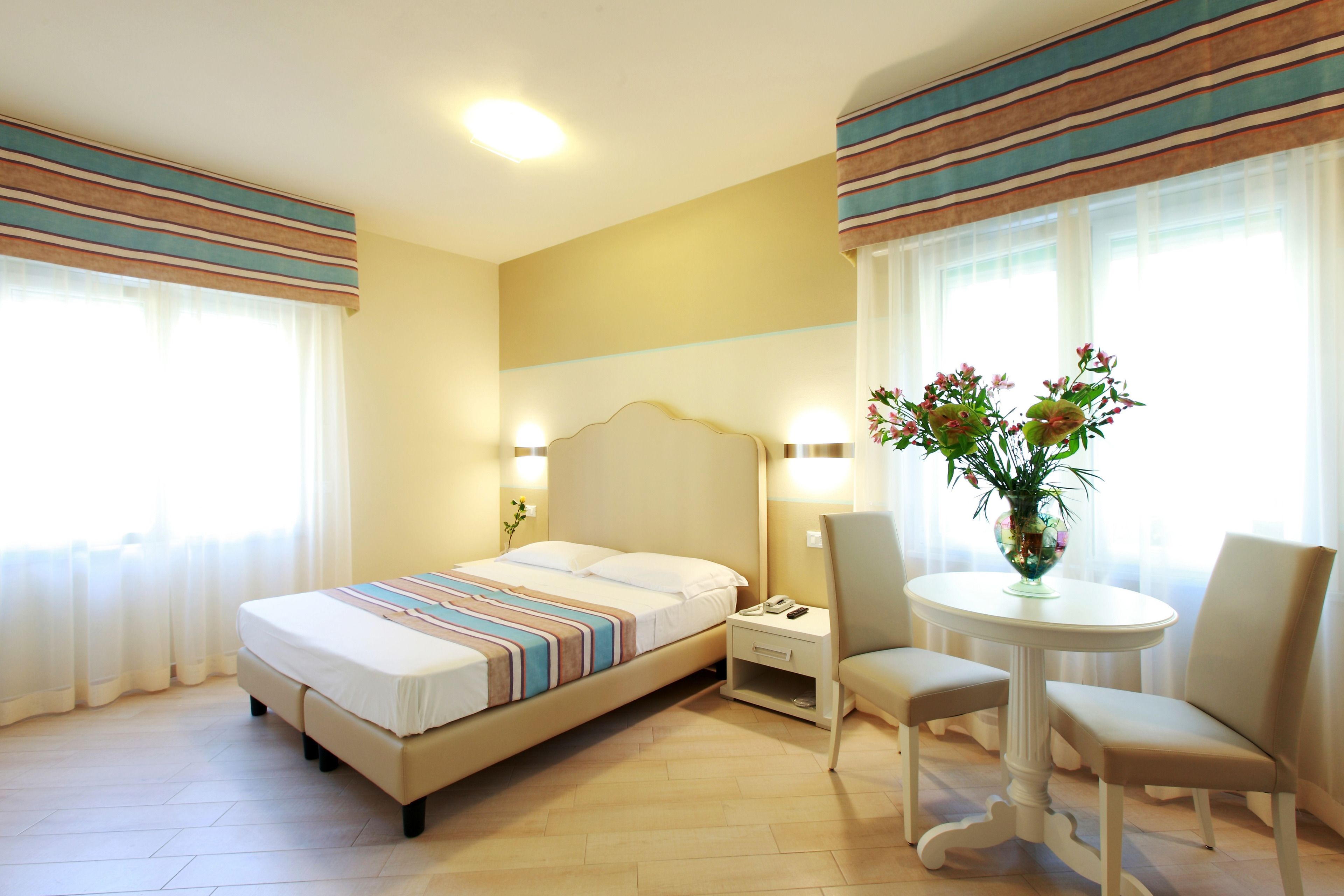 Ein Hotelzimmer mit Bett, Nachttisch, Stuhl und einem kleinen runden Tisch mit Blumenvase.