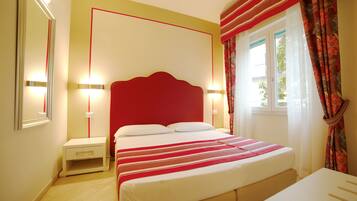 Un dormitorio con cabecera roja, una cama con ropa de cama blanca, una mesita de noche y una ventana con cortinas.