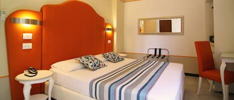 A hotel room with a large bed, a small table, a chair, and a desk.