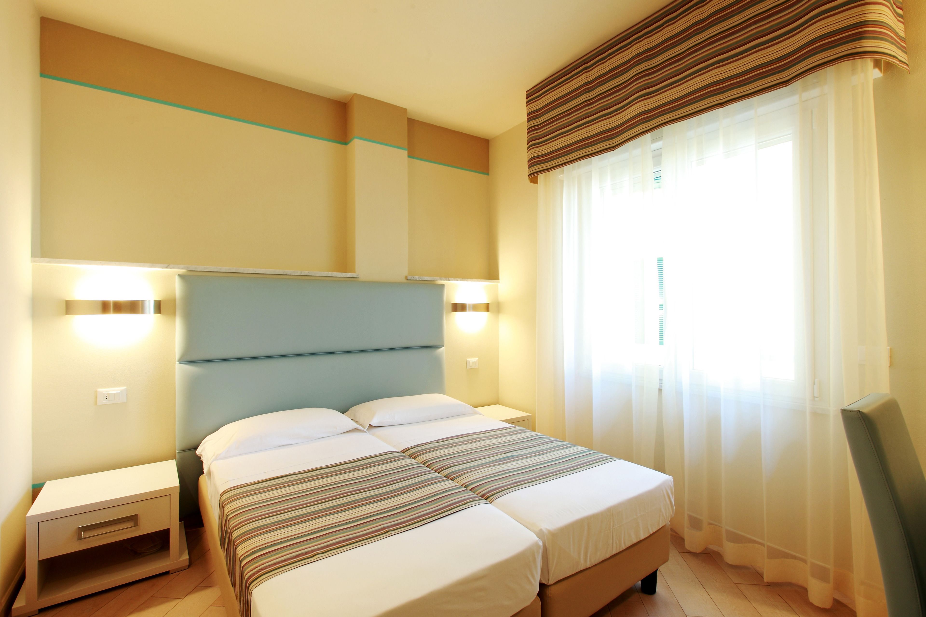 A hotel room with a bed, bedside tables, and a window with curtains.
