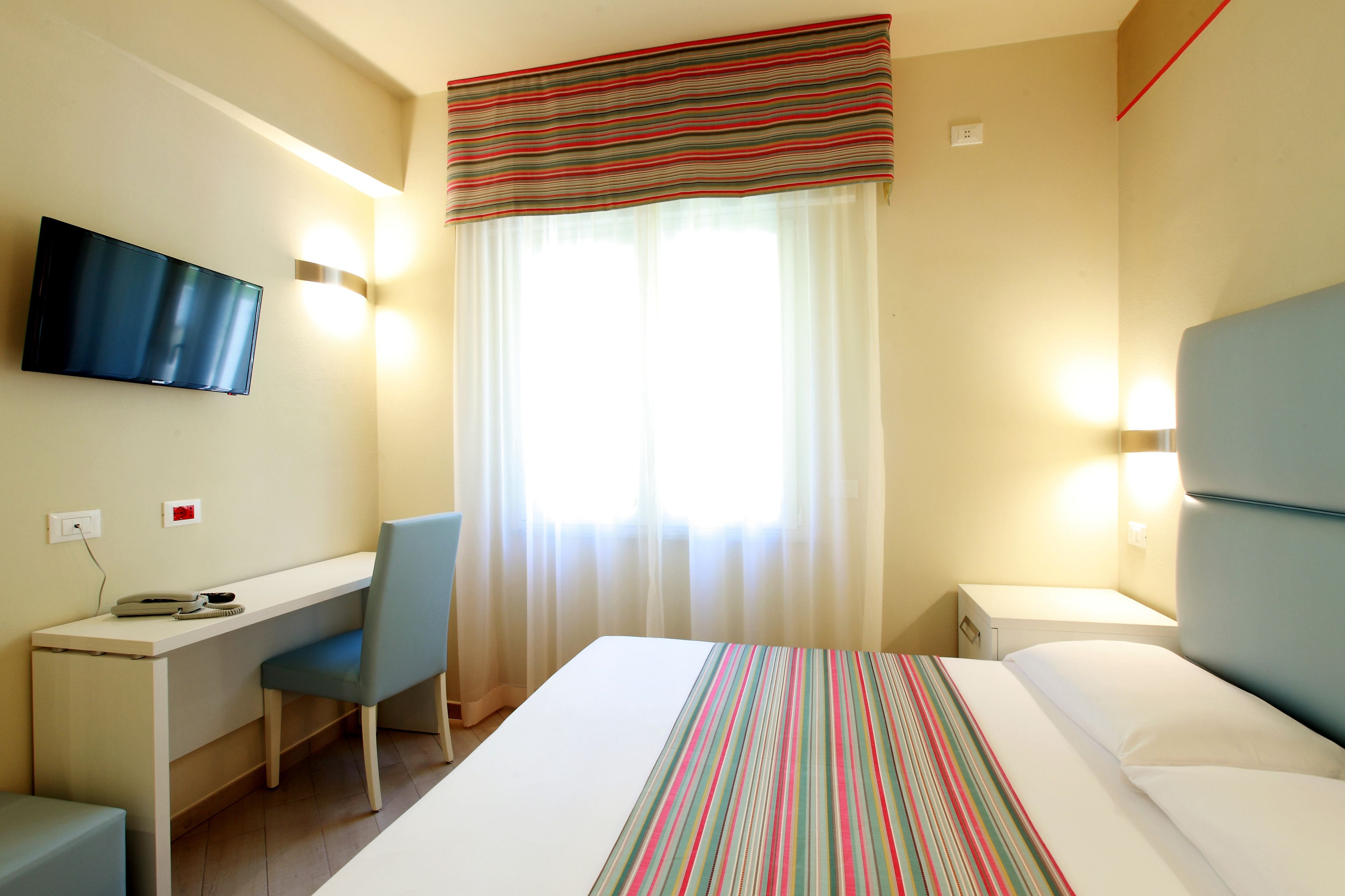 A hotel room with a bed, a desk, a chair, a television, and a window with curtains.