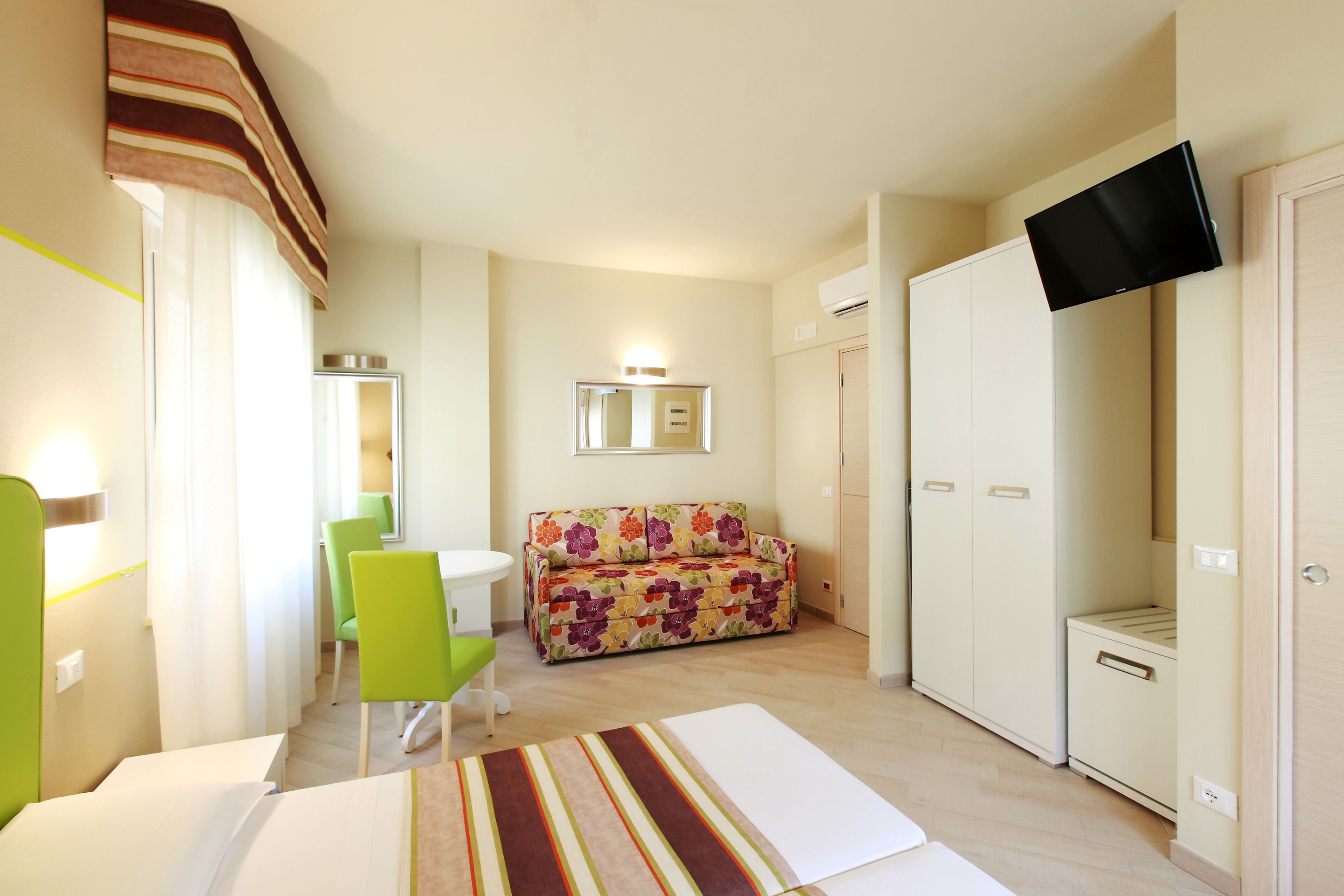 A hotel room with a sofa, a TV mounted on the wall, a small table, and a chair.