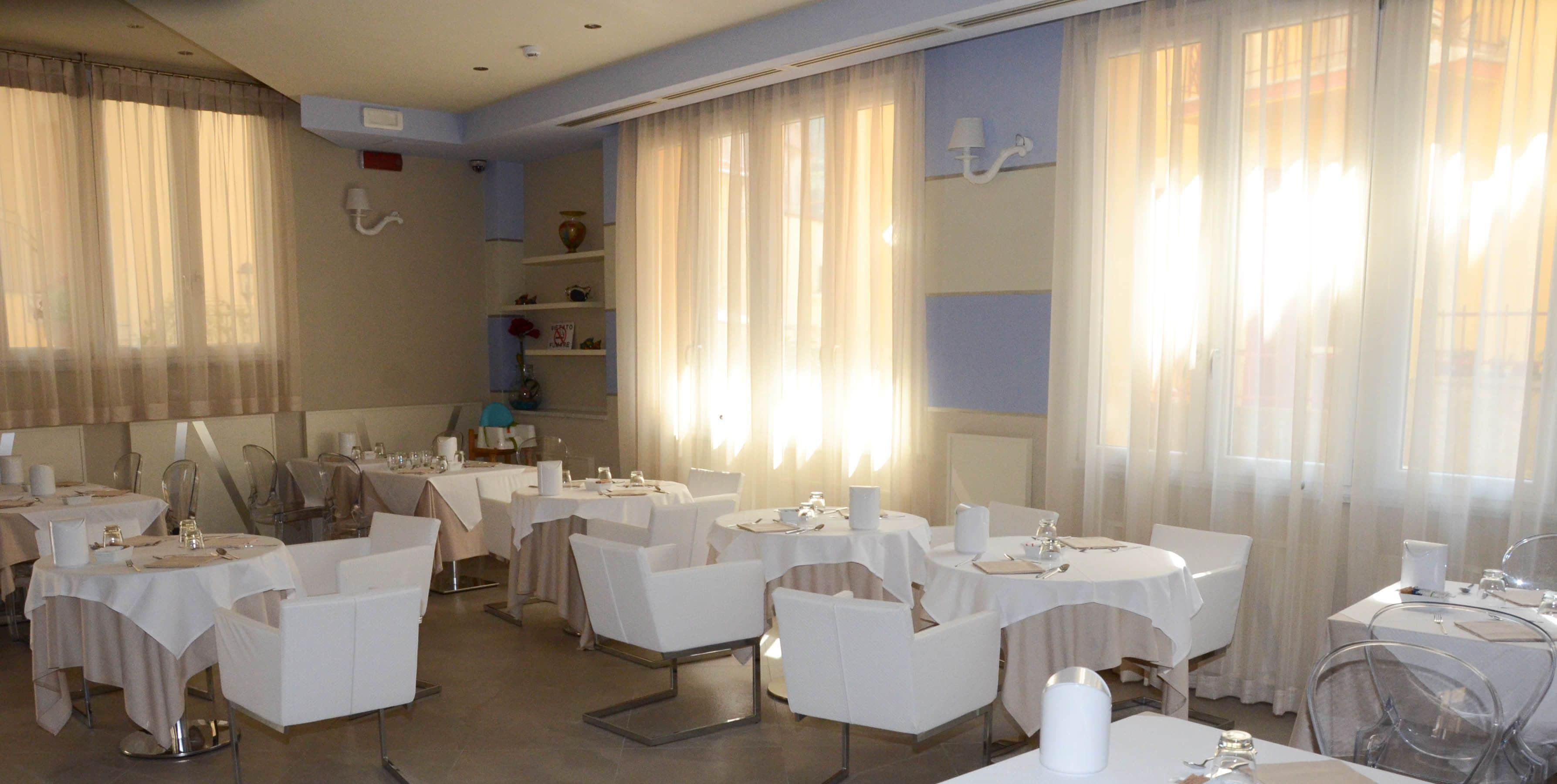 Un espace repas avec des tables rondes, des chaises blanches et un buffet.