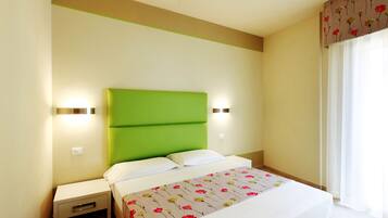 Una habitación de hotel con cabecera verde, ropa de cama blanca y una colcha estampada con motivos florales.