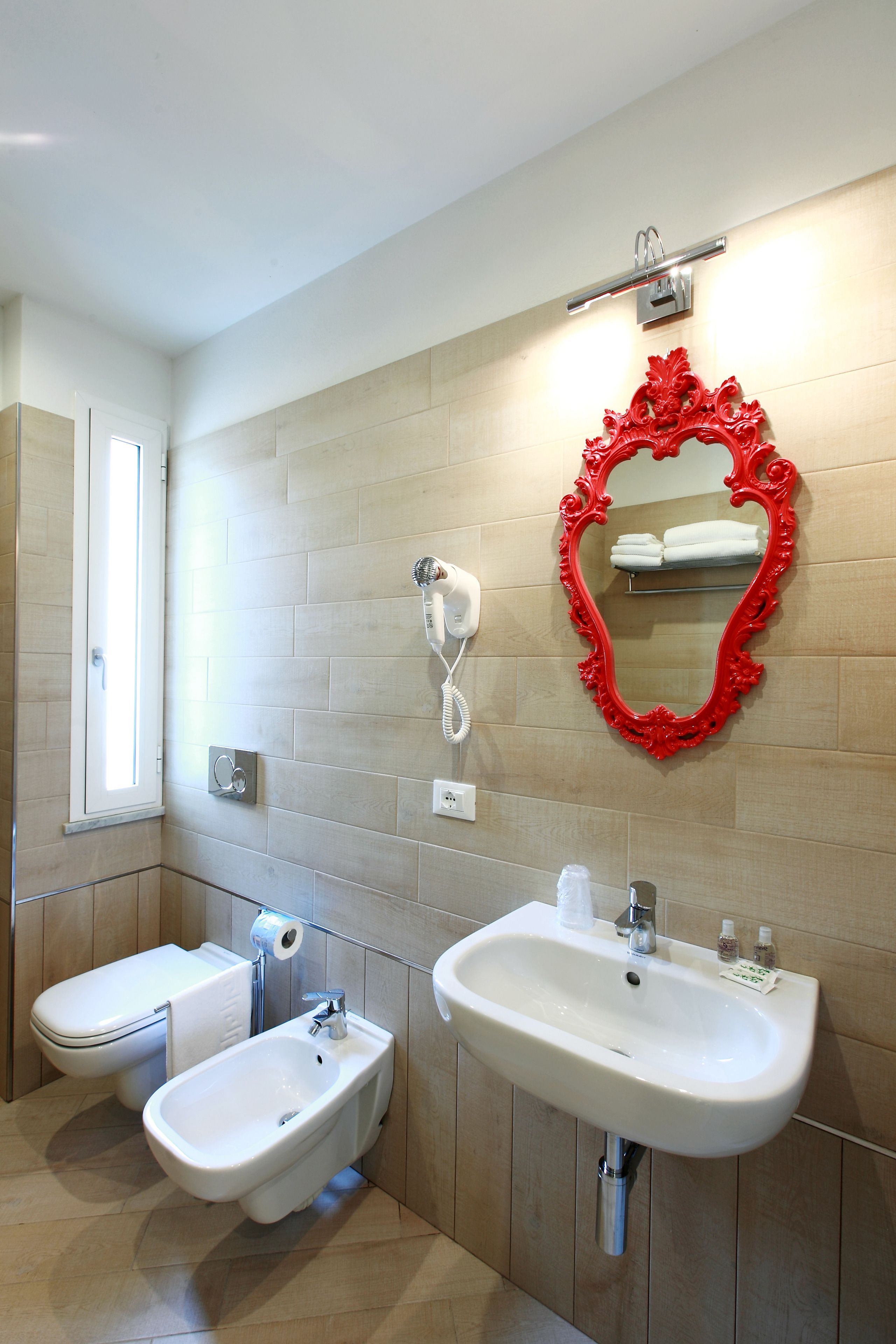A modern bathroom with a bidet, a sink, and a mirror with a red frame.